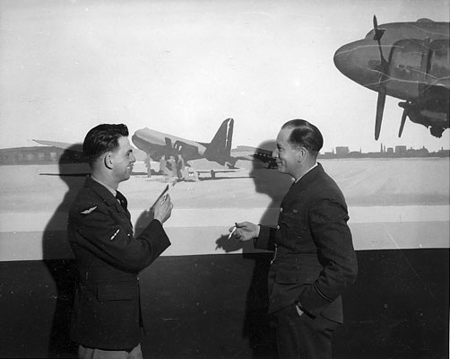LAC J. B. Taylor with unknown man in front of mural of Edmonton Airport, in Officer's Lounge, North West Air Command, Edmonton. c.1945.